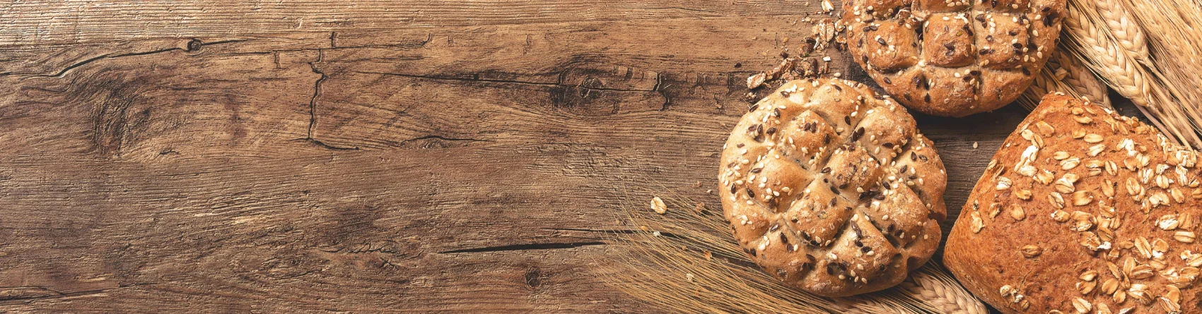 Assorted whole-grain bread loaves and wheat stalks on a rustic wooden surface.